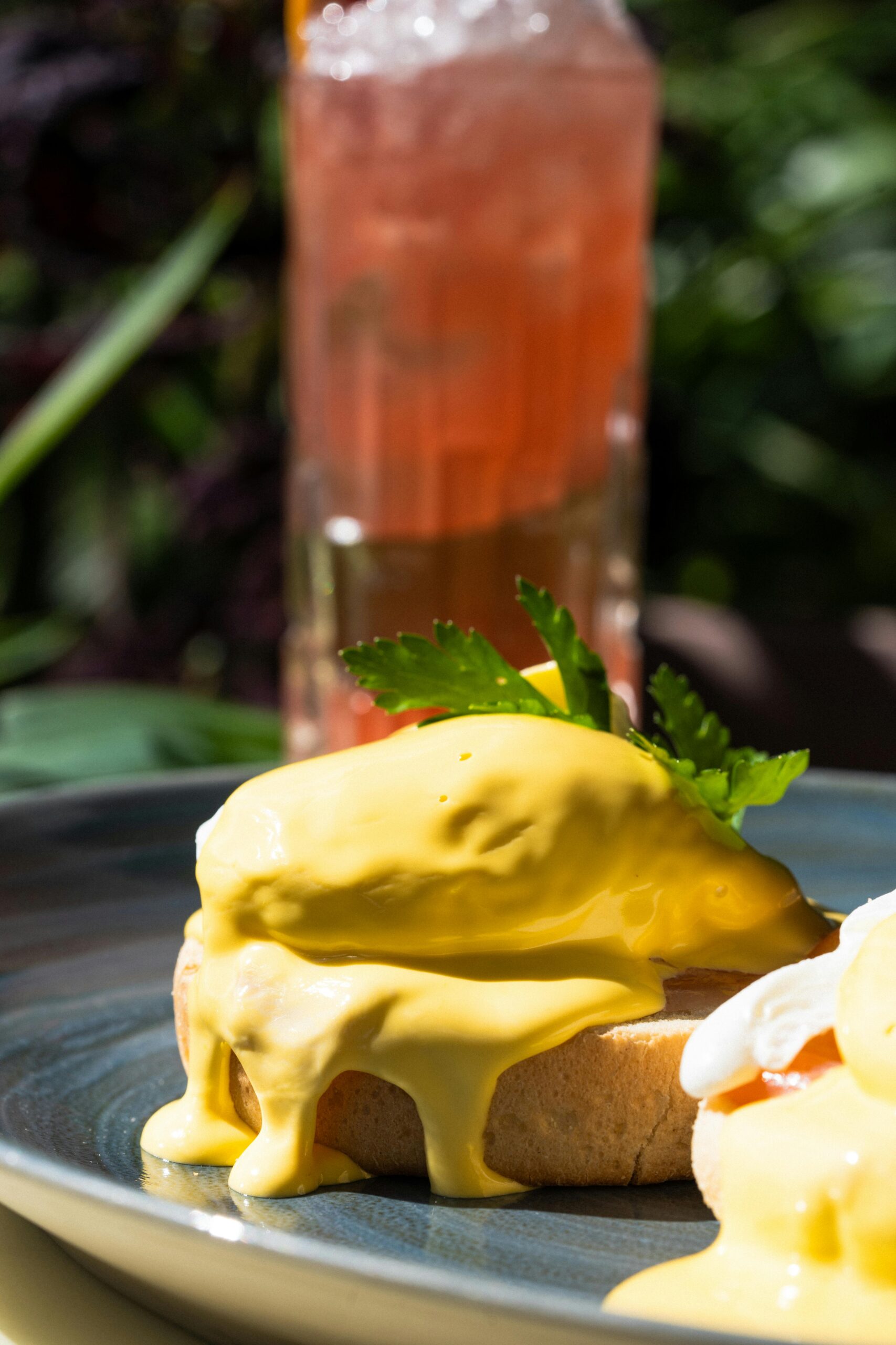 Close-up of eggs benedict with hollandaise sauce and a refreshing drink outdoors.
